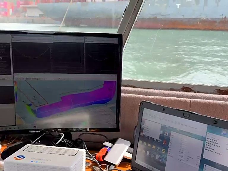 Superficie multihaz en el monitor de a bordo, con un buque atracado al otro lado de la ventana